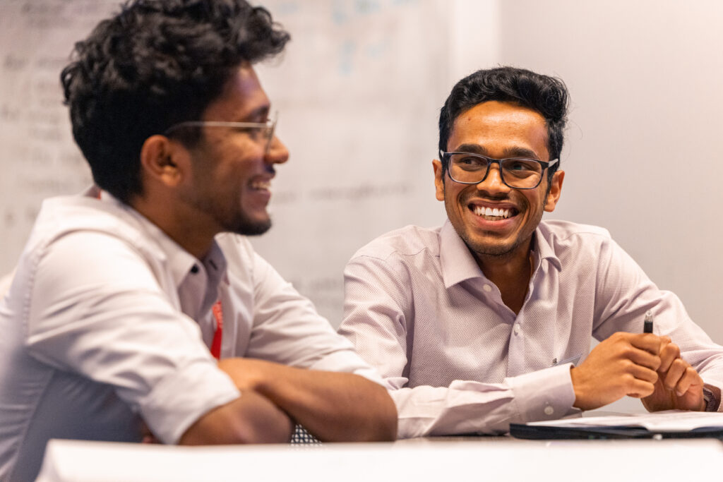 2 students at the hackathon event sitting at a table laughing.